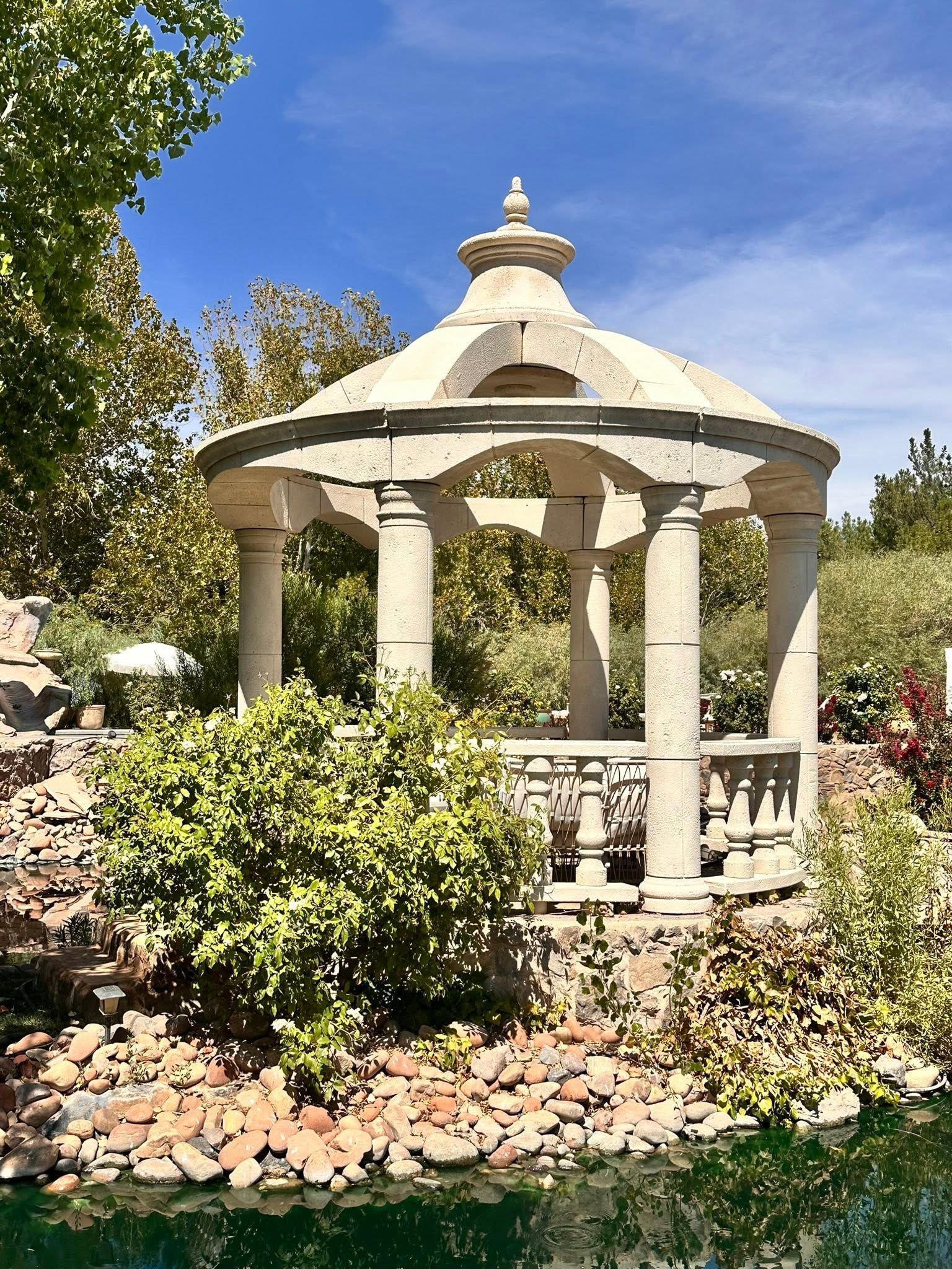 A round foam gazebo with a domed roof, columns, and a turned balustrade by a pond