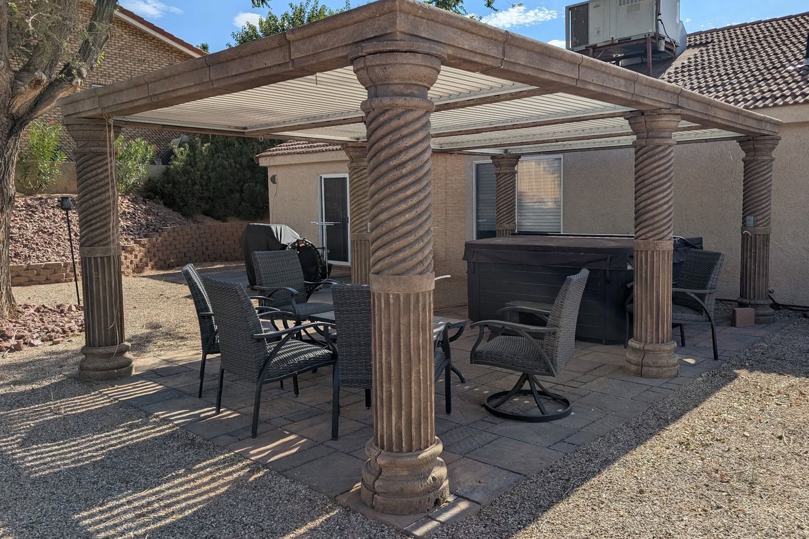 A backyard pergola on foam columns shading a paver patio and hot tub