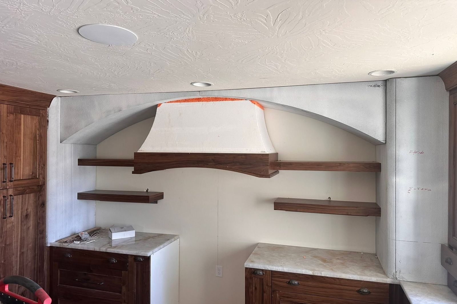 A foam range hood and arched soffit installed above walnut shelving